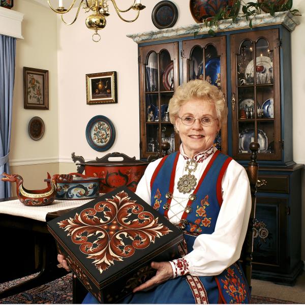 Eldrid Skjold Arntzen wearing traditional Norwegian clothing and holding a box with her floral designs painted on it. 