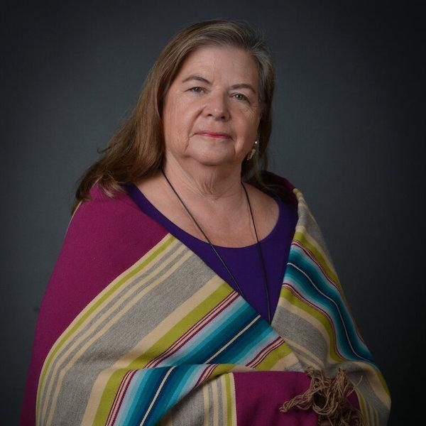 A woman with brown and grey hair is wrapped in a multicolored striped shawl 