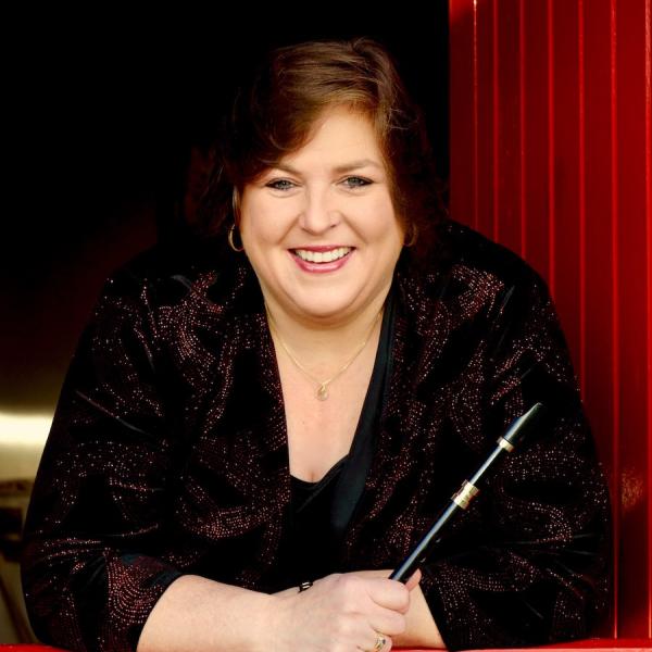 A woman with dark hair holds a black Irish whistle and leans against a latched red wooden half door