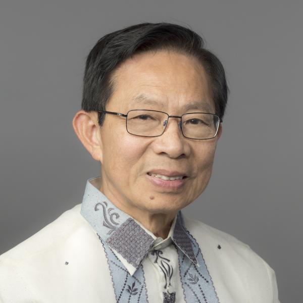 A man with dark brown hair and glasses wears a white, light blue, and grey collared shirt