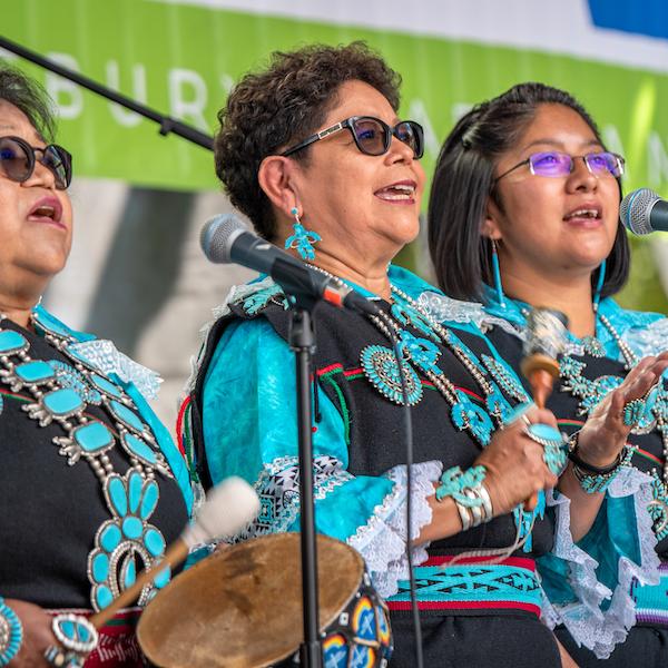 Three women singing from a stage.
