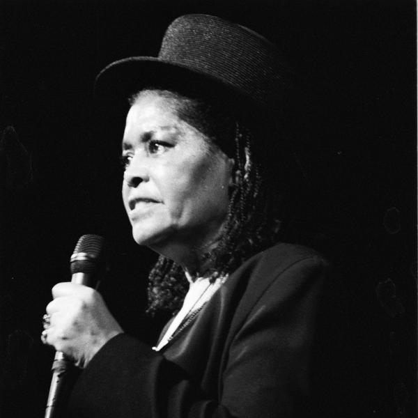 Woman in top hat holding mic on stage. 