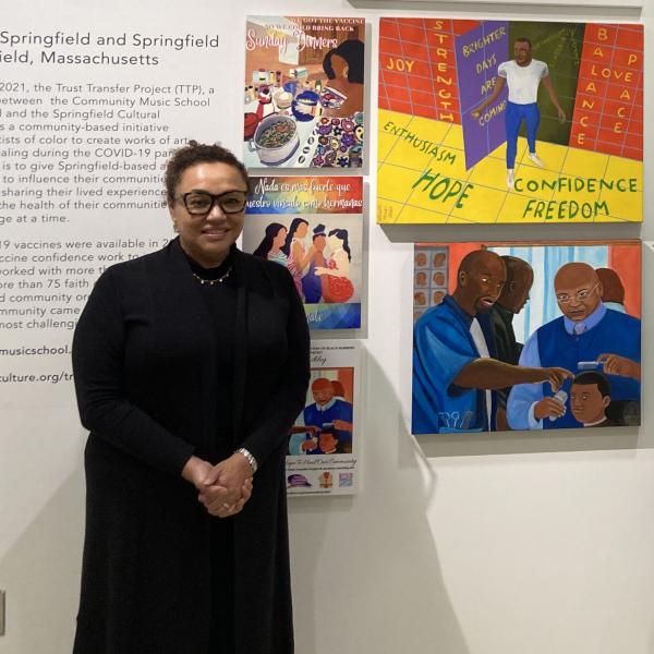 Woman in black dress wearing glasses standing in front of artwork at museum. 