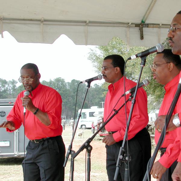 Five men wearing red shirts on stage singing. 