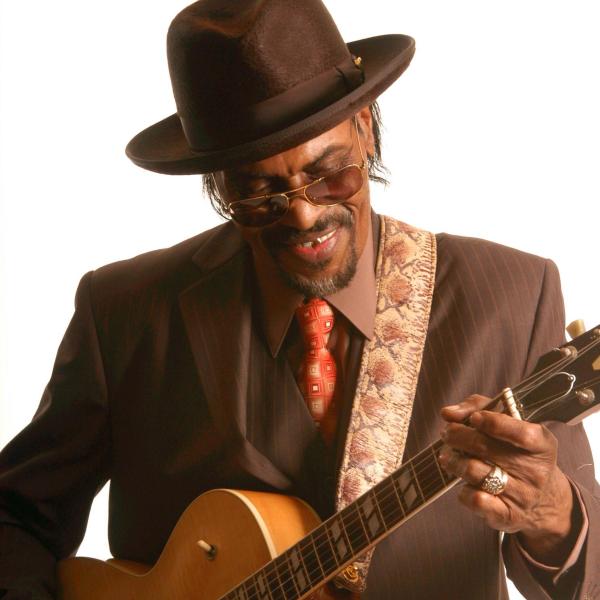 Man in hat and suit playing guitar.