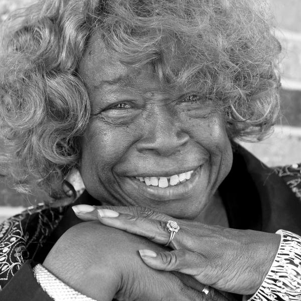 Portrait of Black woman with medium length curly hair smiling, her hands folded under her chin.. 