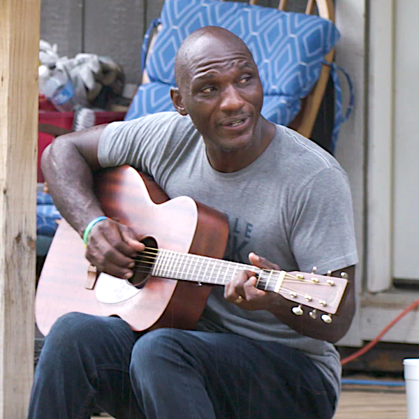 A man sitting on a porch playing the guitar.