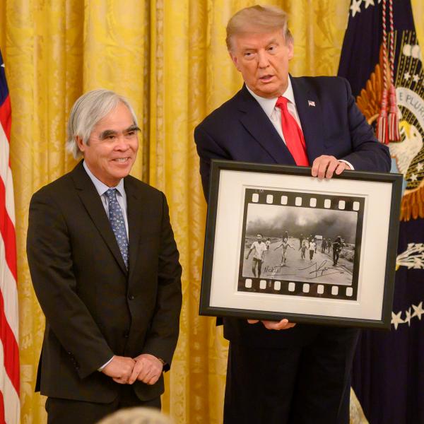 Man holding photo next to man by US flag.