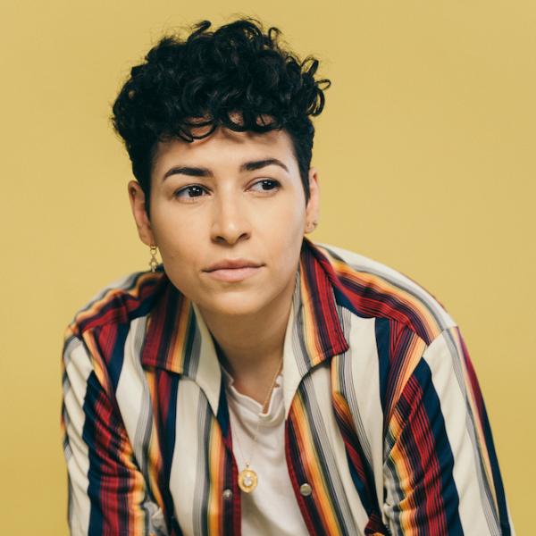 Denice Frohman, who is a woman with curly hair. She is seated and wearing a colorful striped shirt
