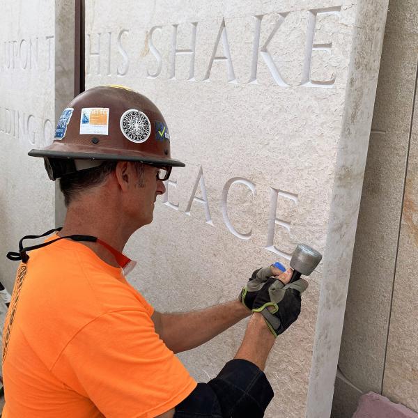 Man in hardhat and yellow shirt etching into stone. 