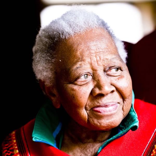 An older woman with short white hair and kind eyes looks off to the side and smiles, as if recalling a beautiful story. 