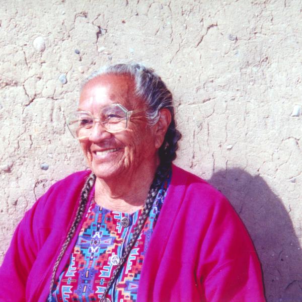 Older woman with gray hair and glasses wearing purple sweater against a white wall
