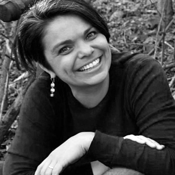 Woman with black hair wearing a dark long-sleeved shirt smiling and posing outdoors. 