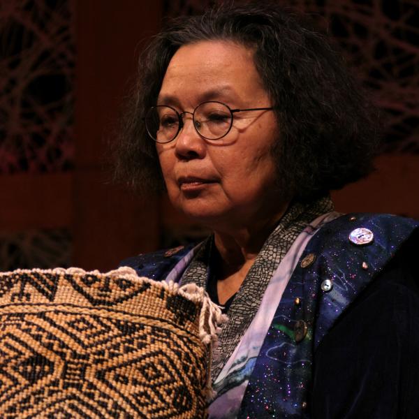 Native woman with glasses holding designed basket. 
