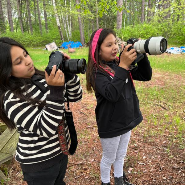 Two students hold large digital cameras in an outdoor setting 