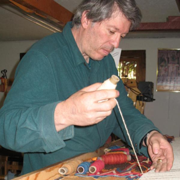 Man in blue shirt at a loom. 