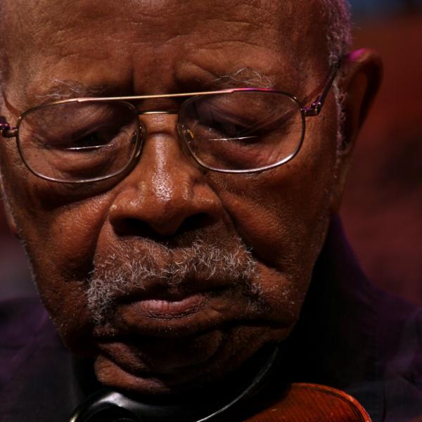 Elderly Black man wearing glasses playing a fiddle.