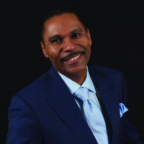 Portrait of a middle-aged Hispanic man with short dark hair and moustache wearing a blue suit.