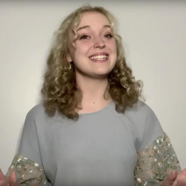 Woman in grey top smiles as she recites to camera with palms facing out