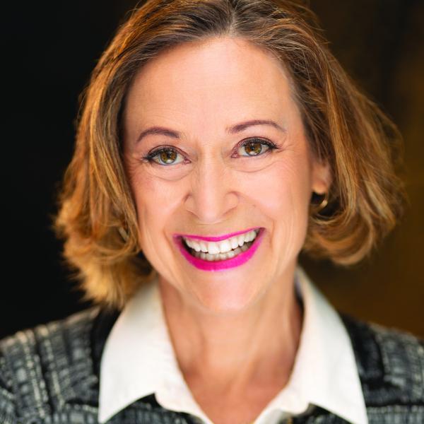 Portrait of a woman with short brown hair, smiling, wearing a blue striped sweater over a white shirt. 