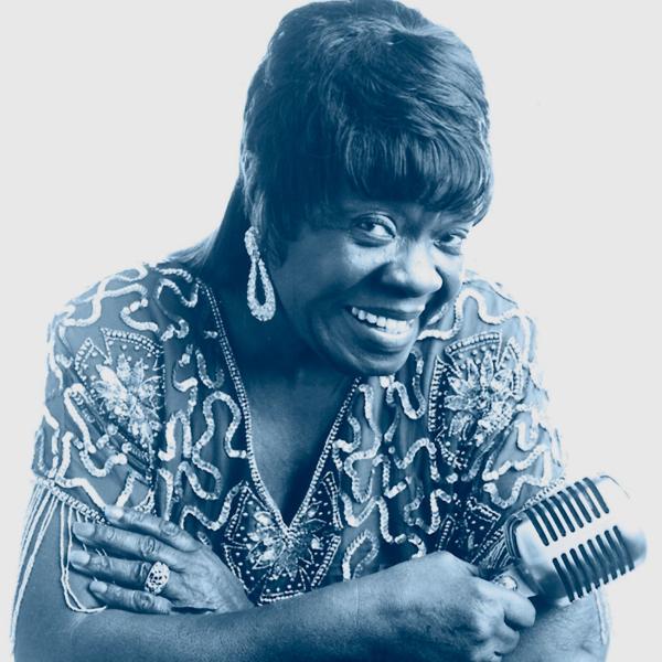 A woman holding a microphone looks at the camera.