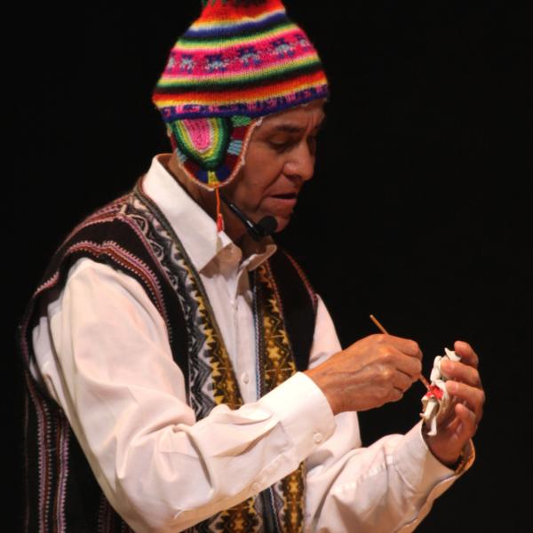 Man wearing a colorful Peruvian hat and vest painting an icon in his hand. 