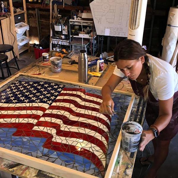 a woman working on a glass mosaic portrait of a rippling US flag