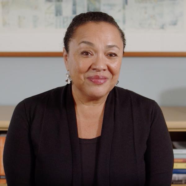 Woman with pulled back black hair and wearing a dark suit in front of a bookcase.