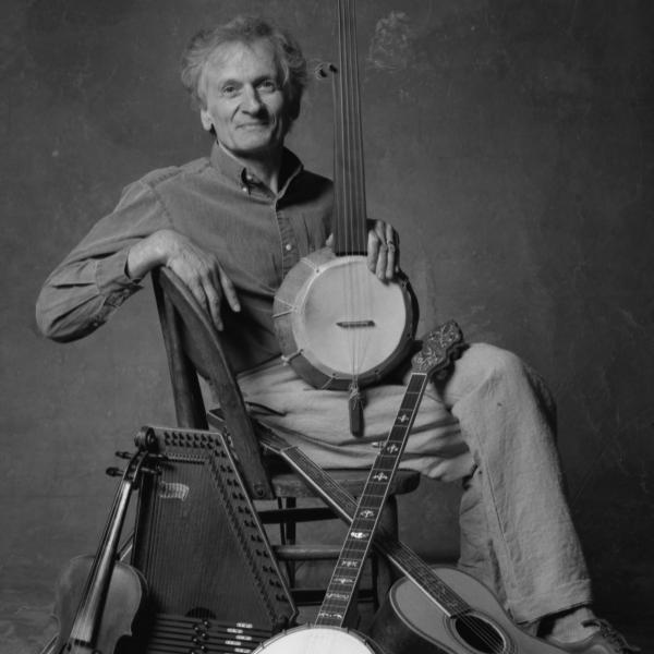 Man sitting in wood chair surrounded by string instruments. 