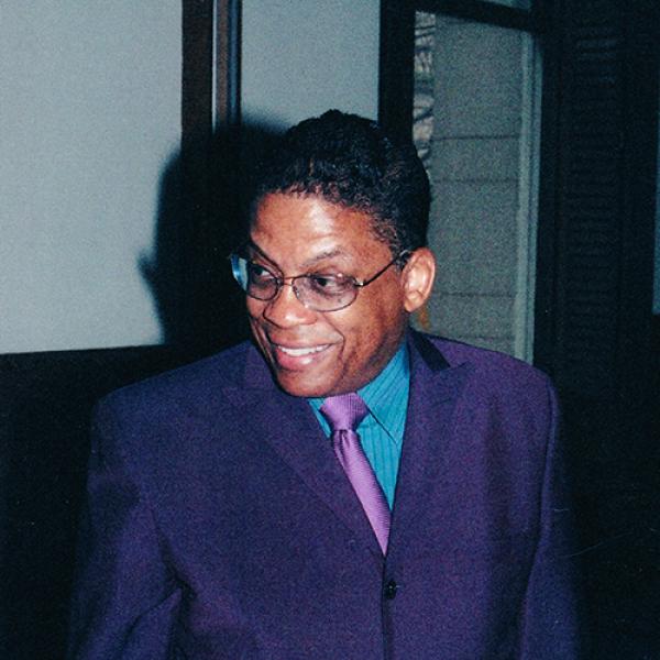 Man in purple suit, smiling. 