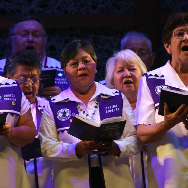 A group of women and men in robes holding hymn books singing. 