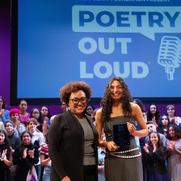 Two women, one middle aged and one teenaged, stand side by side smiling. The teenager holds an award