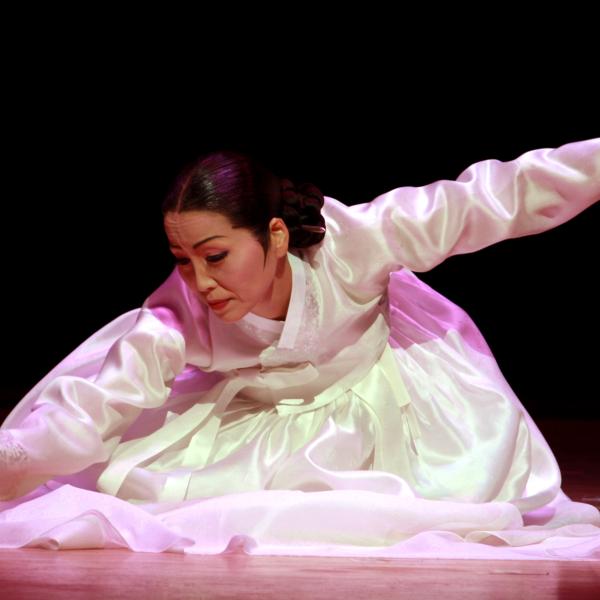 Asian woman with black hair tied back in a white dress in a dance position. 