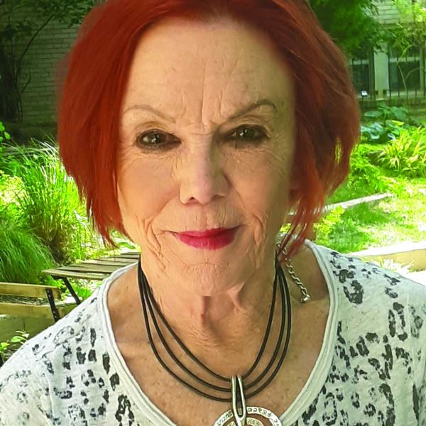 Portrait of an older woman with red hair wearing a lacy top outdoors. 