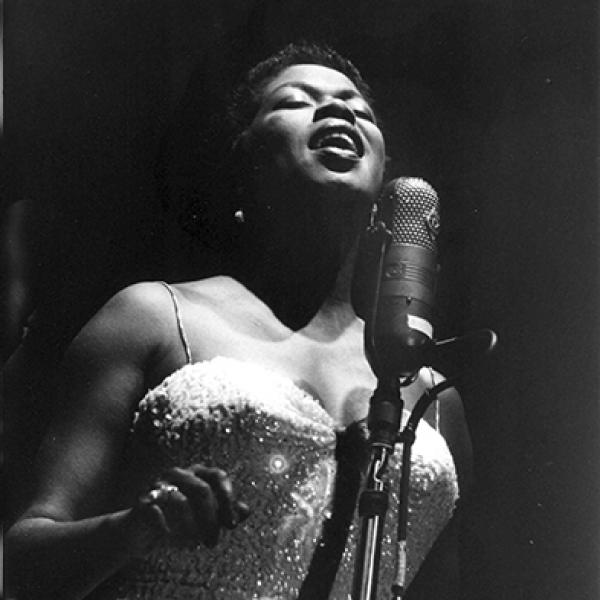 Woman singing at mic on stage. 