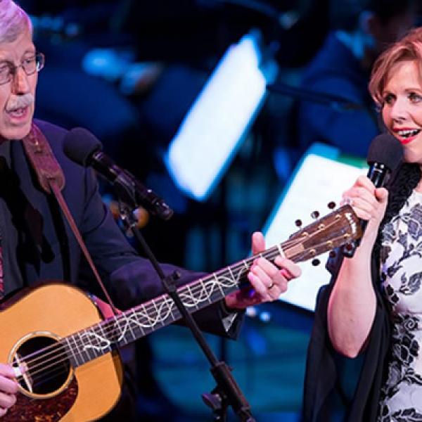 An older man playing a guitar next to a woman singing