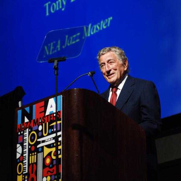 Tony Bennett stands smiling behind a lectern with the NEA Jazz Masters logo 