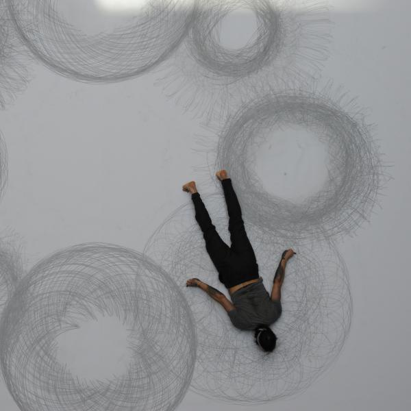 Man lying on paper with charcoal and drawing circles.