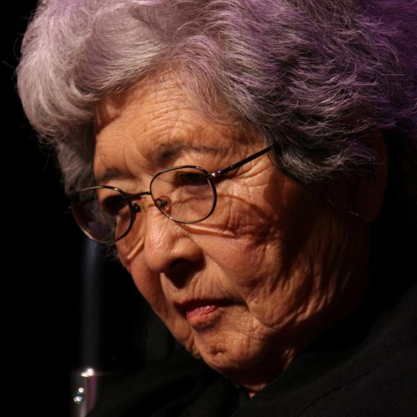Japanese woman with gray hair and glasses looking down. 
