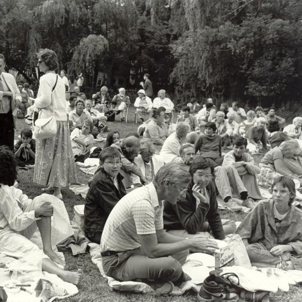 Crowd sitting on lawn for play. 