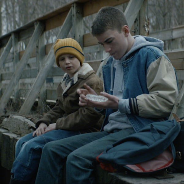 a young boy and a teenage boy sit on the edge of a railroad trestle
