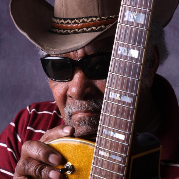 Man holding guitar in cowboy hat. 