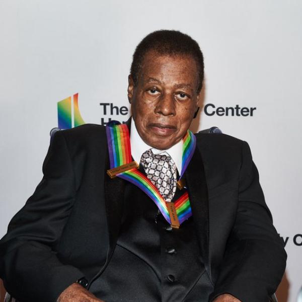 Black man in gray suit in wheelchair with medal with rainbow colored bow around his neck.