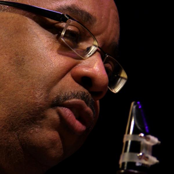 Older Black man wearing glasses holding a clarinet.