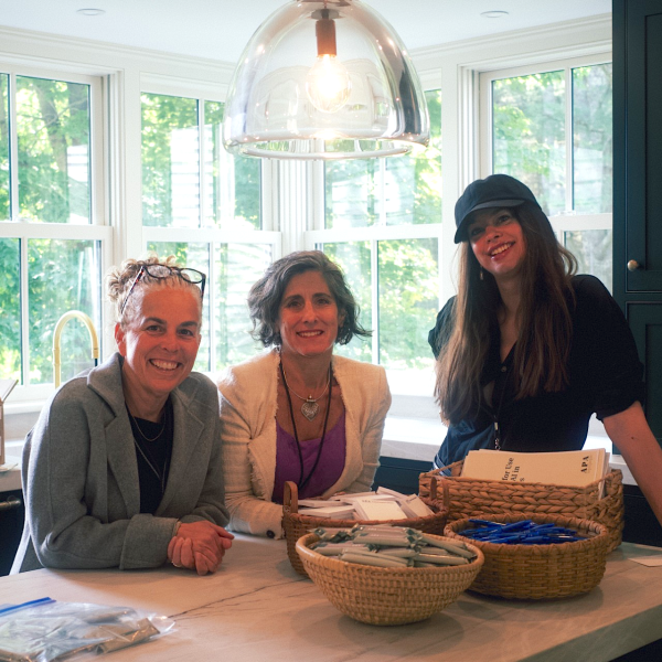 two white women sit around a kitchen table while another stands near the table