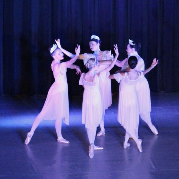 Five young ballerinas dance in a circle on stage.