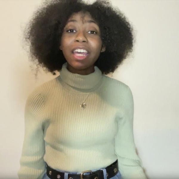 Woman in grey turtle neck looks at camera reciting
