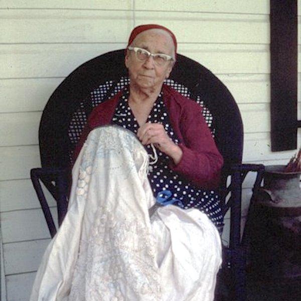 A woman sitting on chair working on a notted bed spread.