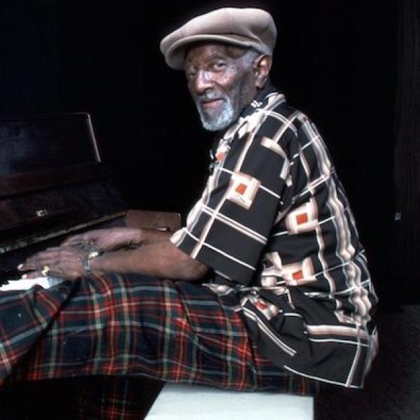 A man playing the piano with a leg up on the keybopard.