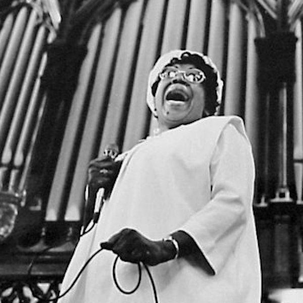 A woman singing in front of a large church organ.